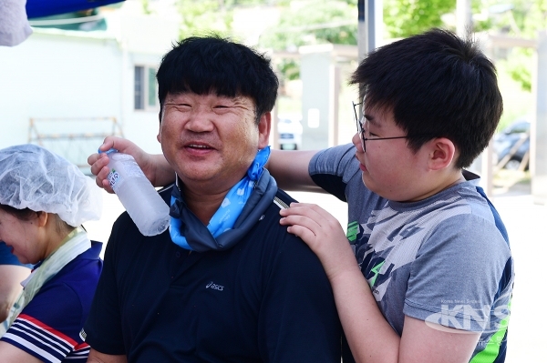 가족과 함께 나온 자원봉사자, 아들이 아버지에게 얼음 생수병으로 더위를 식혀 주고 있다 [ 사진=김준 기자 ]