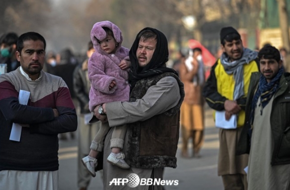 아프가니스탄의 수도 카불에서 딸을 껴안고 여권 발급소에 늘어선 남성(2021년 12월 19일 촬영, 자료 사진). ⓒAFPBBNews